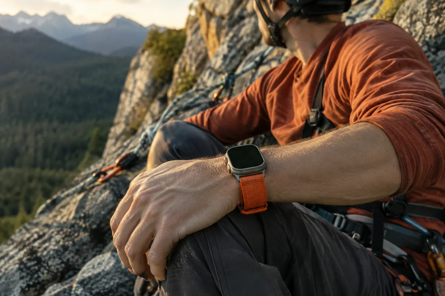 Titánszínű Apple Watch narancsszínű textilpánttal egy felszerelt hegymászó csuklóján.